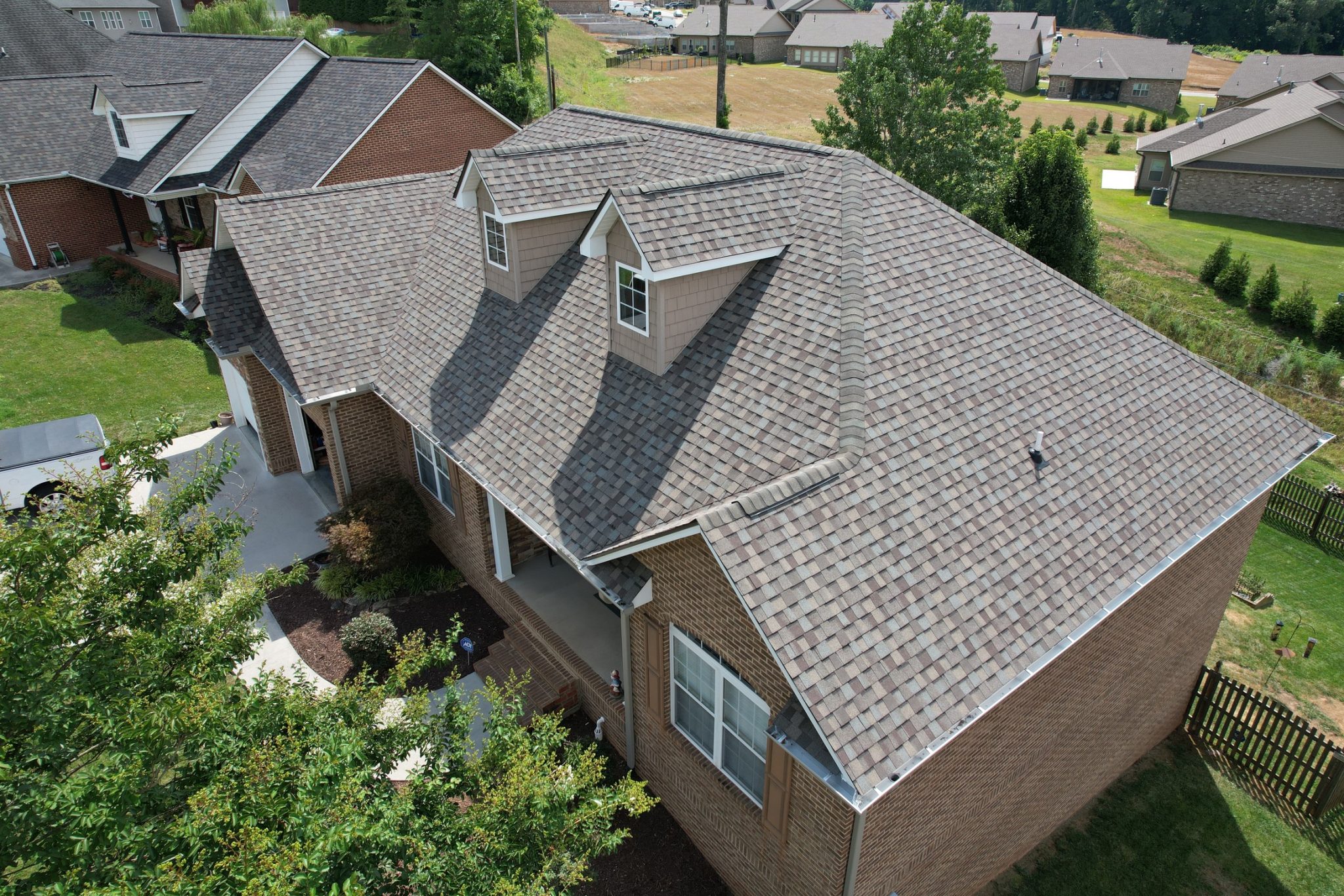 Architectural Shingle Roof on a Brick Home Aerial view of a gray architectural shingle roof with two dormers on a brick-and-siding home.