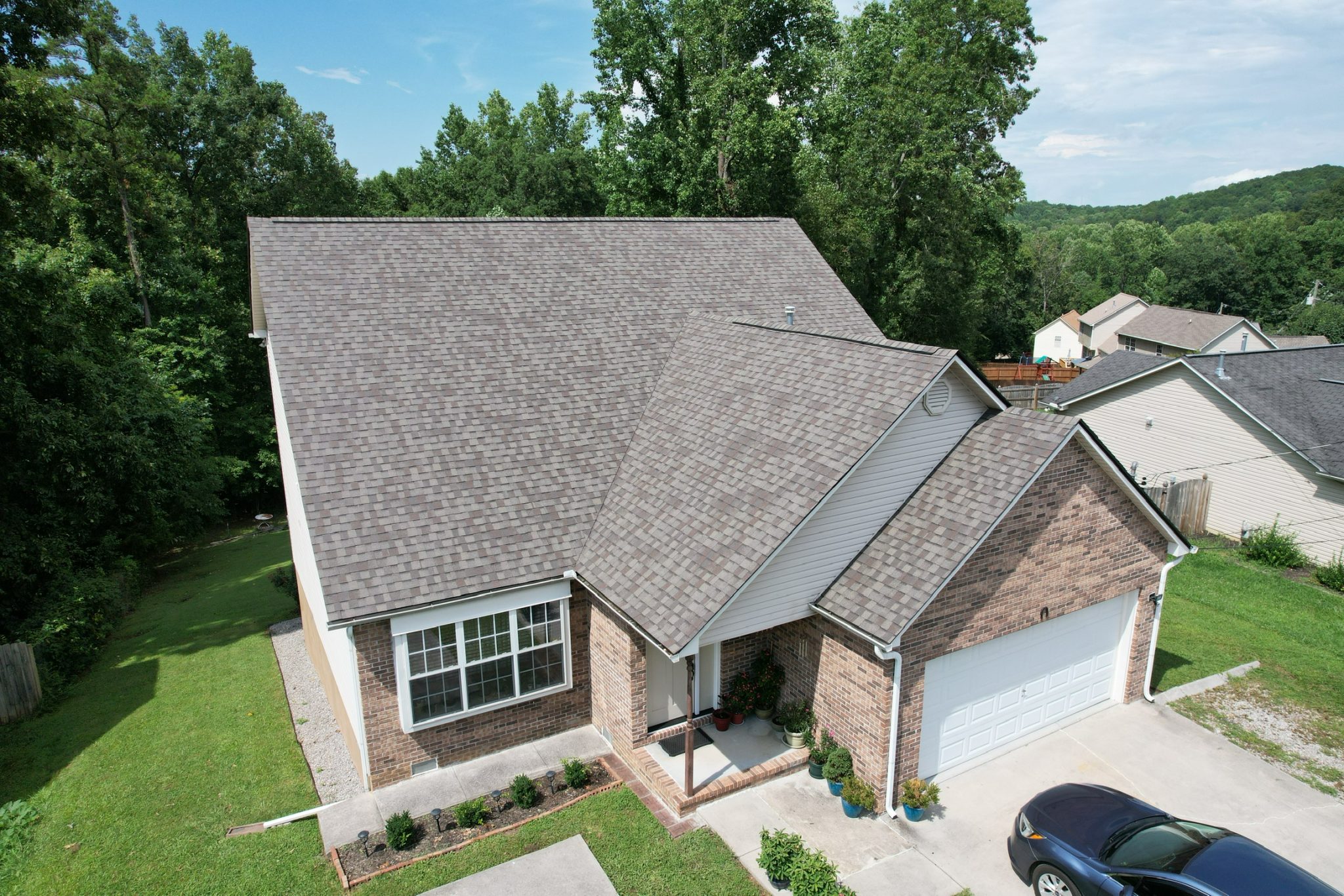 Steep Gable Roof Above a Brick and Siding Home Aerial front view of a home with a steep gray shingle roof and attached garage.