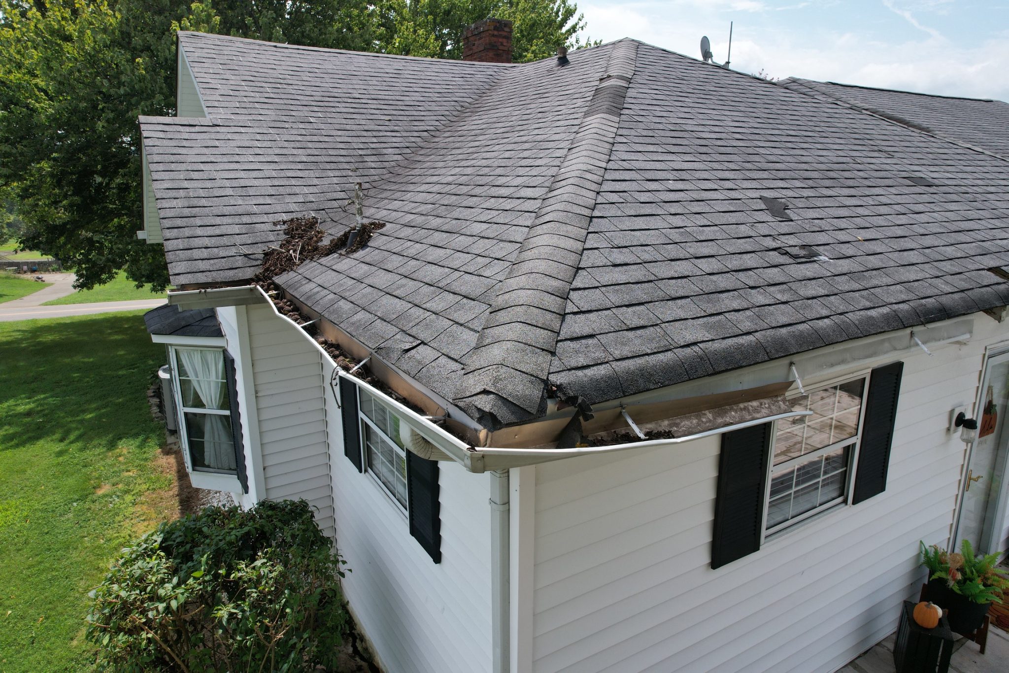 Asphalt shingle roof with curled edges, lifted shingles, and debris in the valley and gutter.