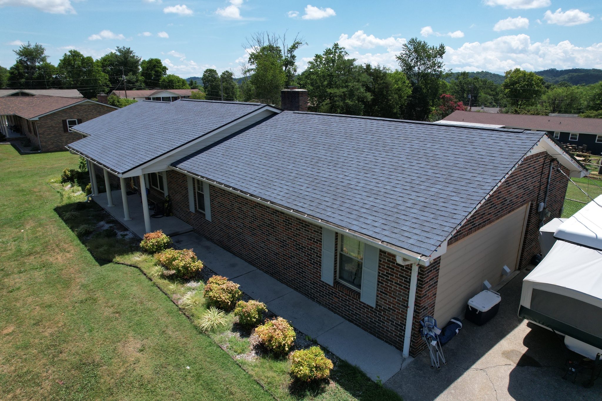 How to Pay for a Roof: Knoxville Asphalt Shingle Roof Replacement. How to pay for a roof illustrated by a new asphalt shingle roof on a Knoxville brick ranch home, aerial view with gutters and front porch under a blue sky.