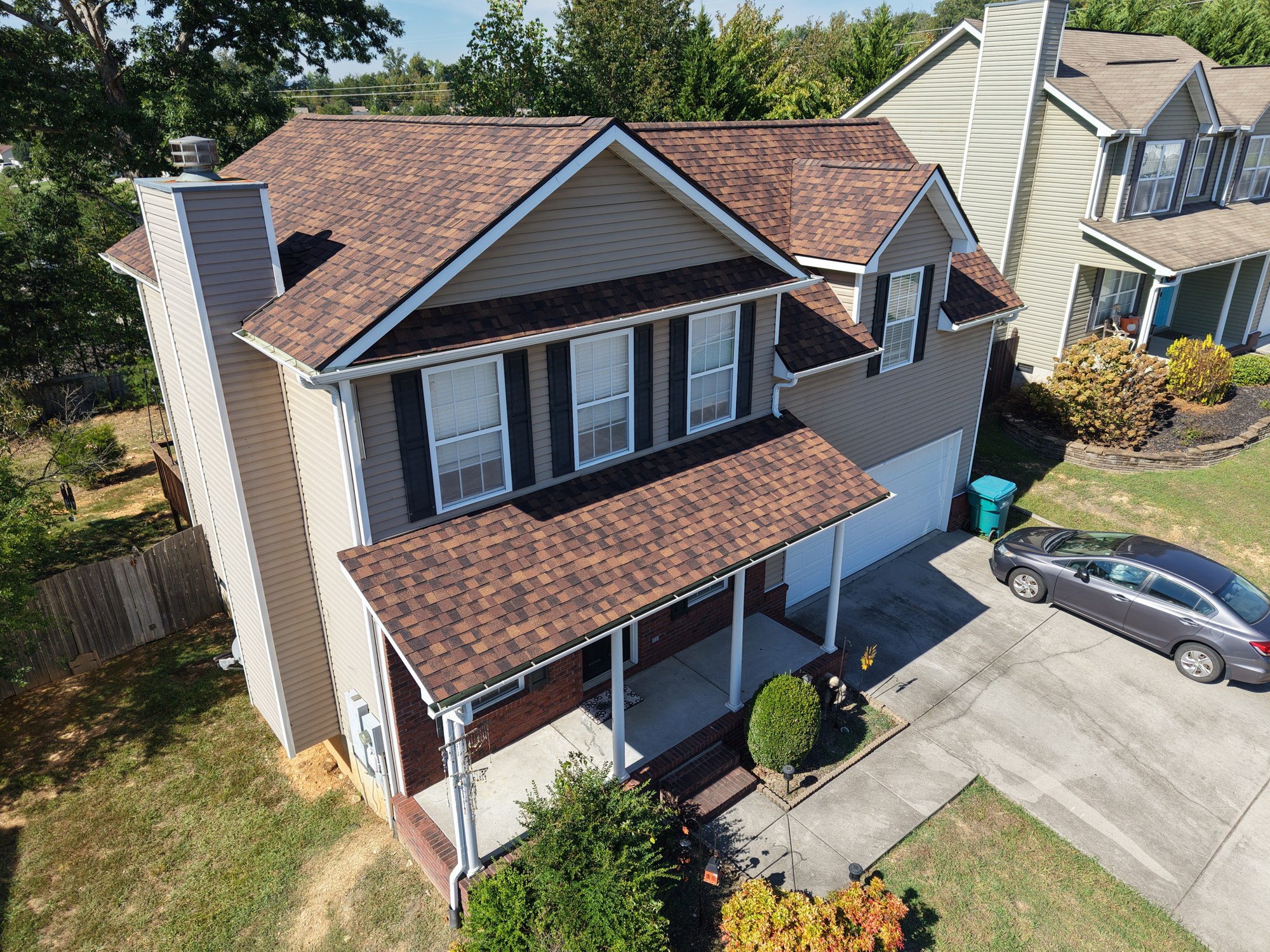 After roof replacement Angled front view of Burnt Sienna shingles above tan siding and a brick porch on a Powell home.