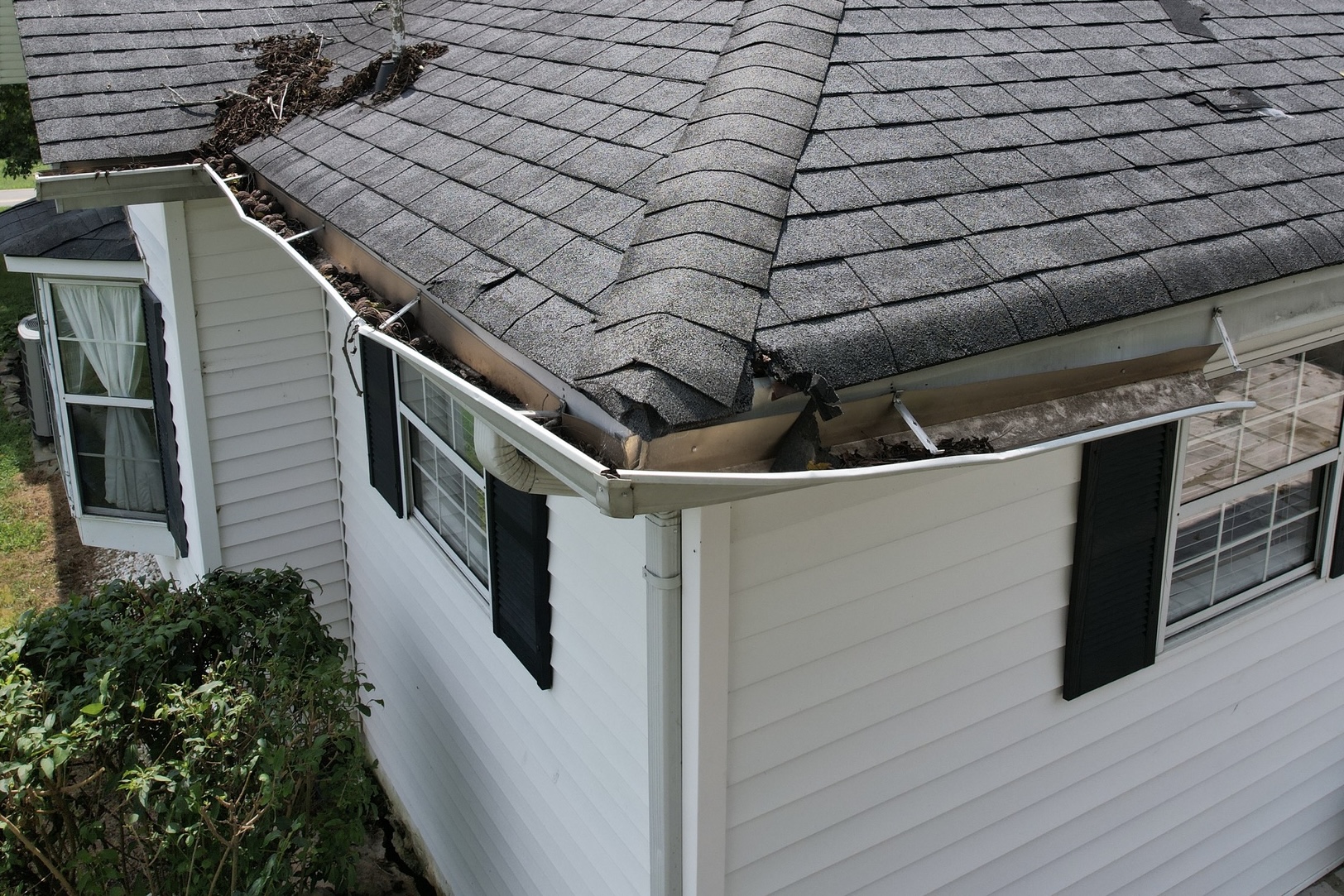 Broken Gutters Needing New Gutters Aerial view of broken, debris-filled gutters pulling from fascia on a white siding home, showing the need for new gutters to stop overflow and protect the foundation.