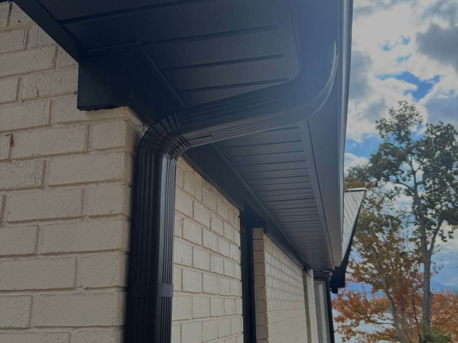 Black gutter and larger rectangular downspout on a brick home, showing 3x4 downspouts for heavy rain. Description: A close view of a brick exterior with a black gutter run and a larger downspout at the corner. The image shows how 3x4 downspouts pair with gutters to move stormwater off the roofline.