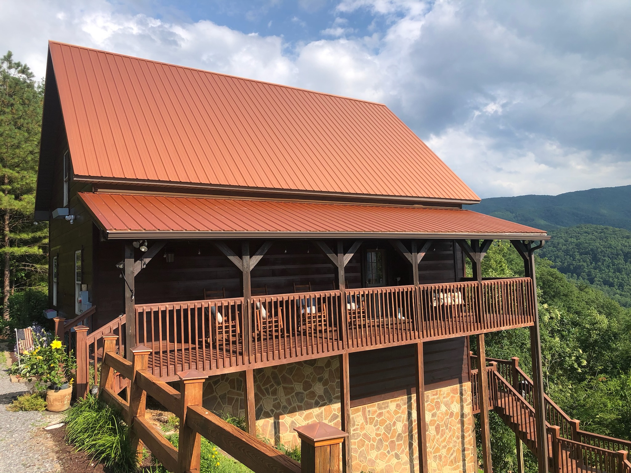 Spring Roof Maintenance for Metal Roofs in East Tennessee A home with a clean red metal roof surrounded by fresh greenery under a bright blue sky.