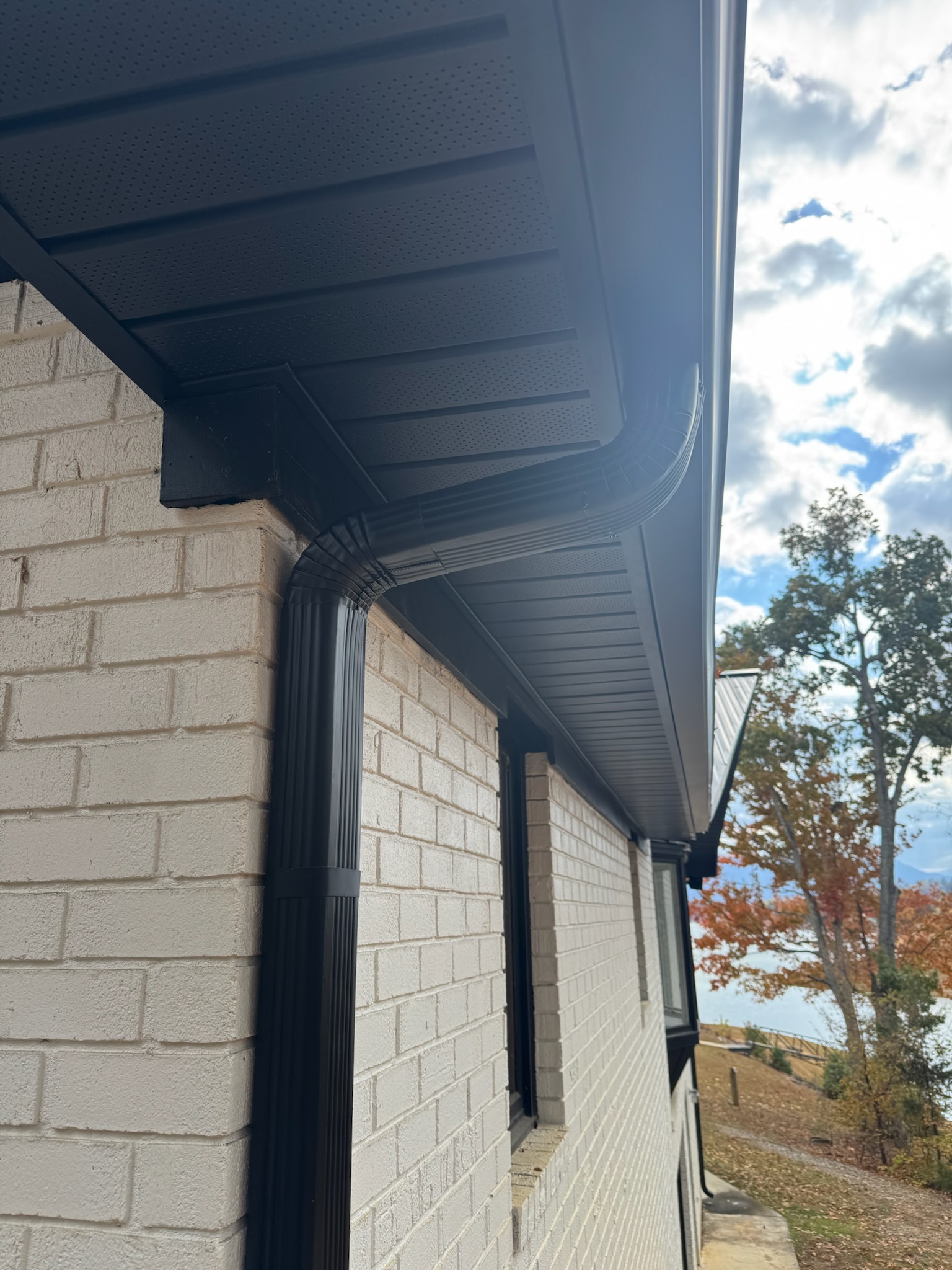 Six-inch seamless gutters Knoxville, TN on modern white brick home Close-up view of six-inch seamless gutters Knoxville, TN installed in black aluminum with matching soffit and downspout on a white brick house.