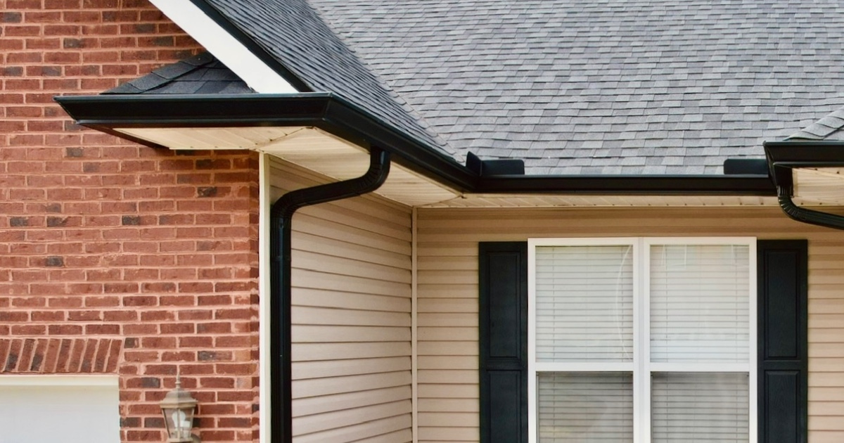 Six-Inch Seamless Gutters on a Knoxville Home. Black Six-Inch Seamless Gutters with a 3x4 downspout on a brick and vinyl Knoxville home, showing clean eaves and corner detail.
