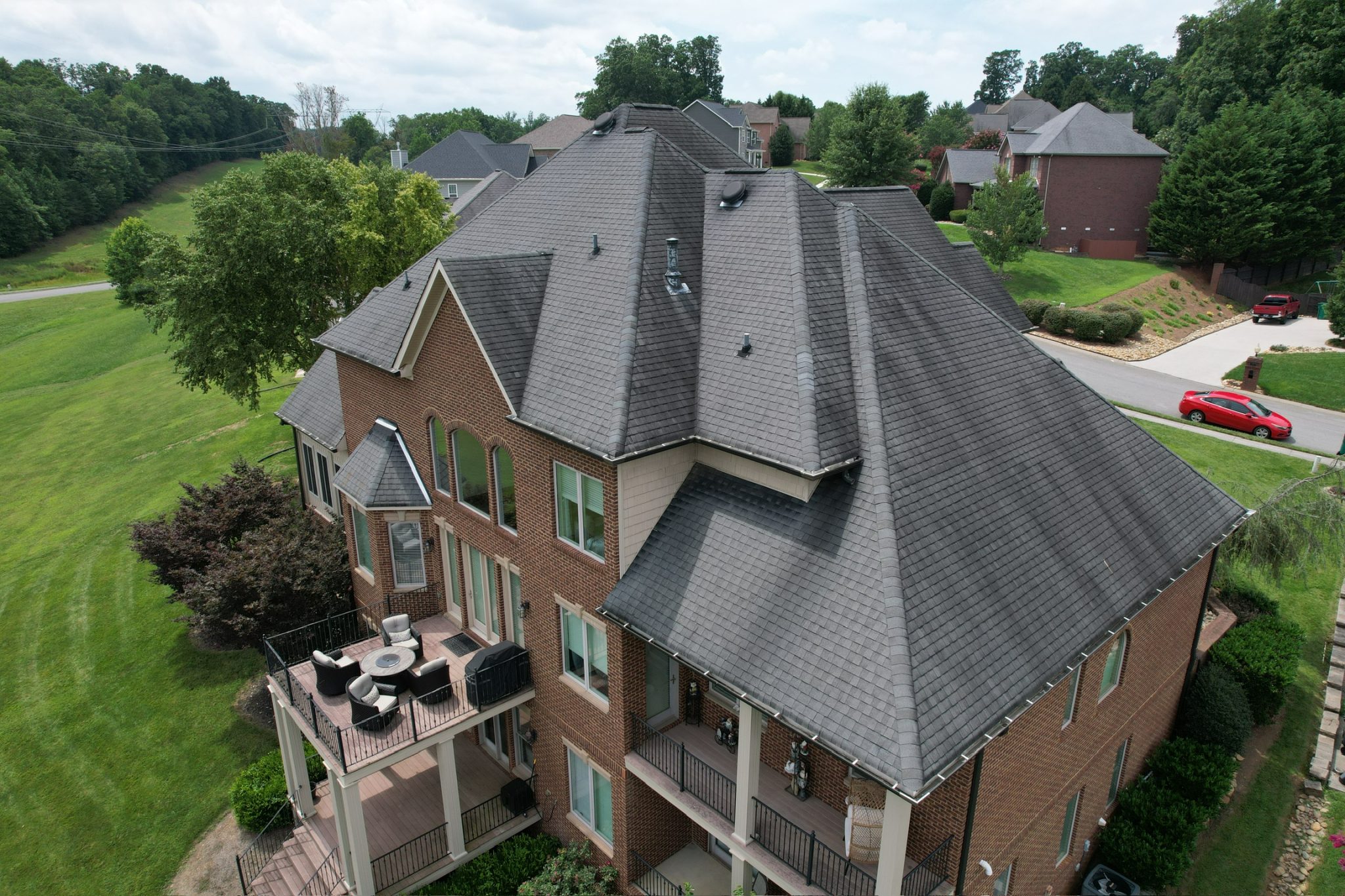 Roof inspection on complex asphalt shingle roof in Knoxville. Aerial photo of a Knoxville brick home during a Roof inspection, showing gray asphalt shingles, vents, valleys, and gutters on a steep multi-gable roof.