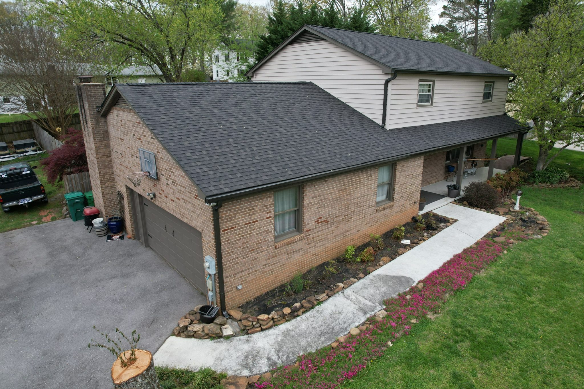 Gutter replacement Knoxville, TN on a brick home with a dark shingle roof, black gutters, and downspouts by the driveway.