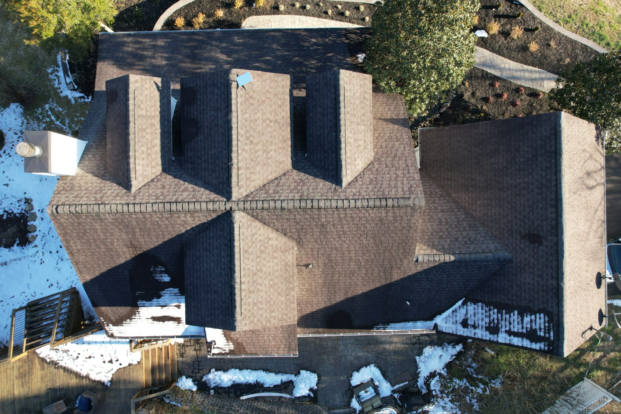 Heat Bills Climbing: How a New Roof Helps in Cold Snaps Aerial view of an asphalt shingle new roof in winter, with patchy snow that highlights heat loss during a cold snap.
