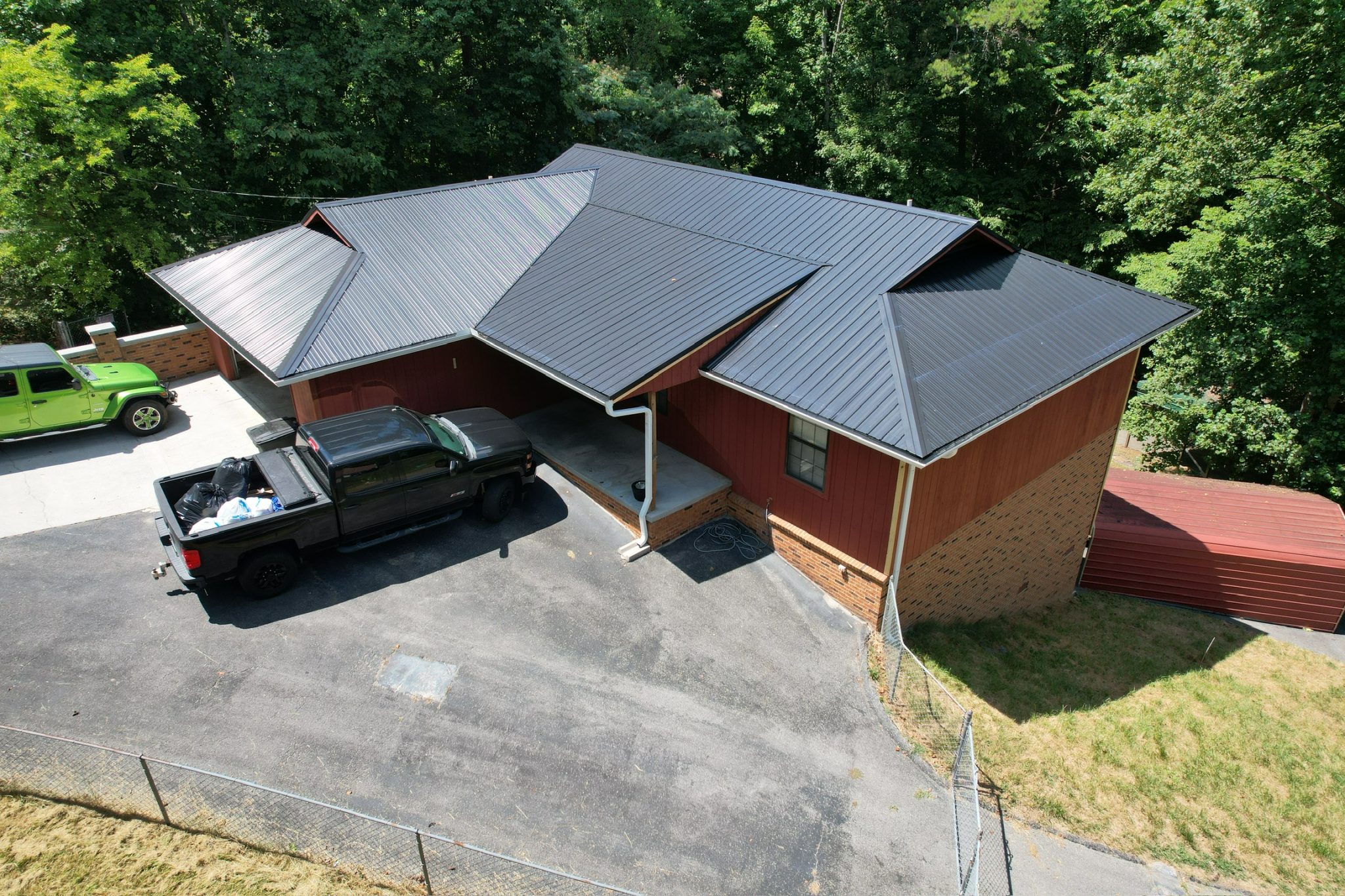 Knoxville Home Showing Metal Roofing Energy Savings in Summer. Aerial view of a Knoxville, Tennessee home with a dark standing seam metal roof and shaded lot, illustrating metal roofing energy savings during hot summer months.