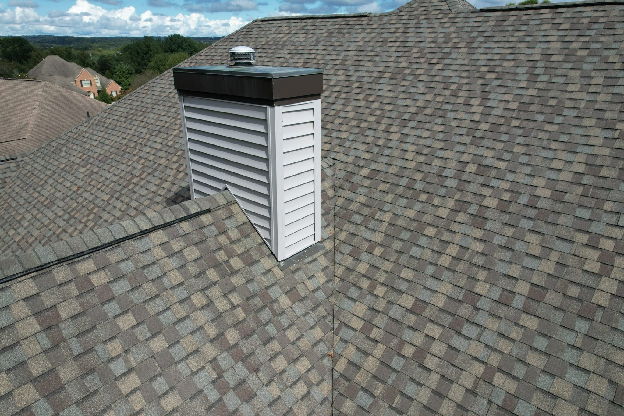 Architectural Shingles vs 3-Tab for East Tennessee Roofs Architectural Shingles vs 3-Tab roofing view with multi-tone asphalt shingles around a chimney chase and roof valley.