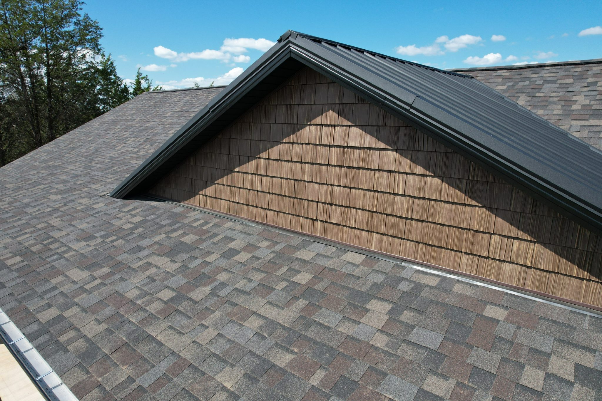 What Our Roofing Warranty Covers (and Why It Matters) Architectural asphalt shingles with a metal accent dormer on a clear day, showing a system backed by our roofing warranty.