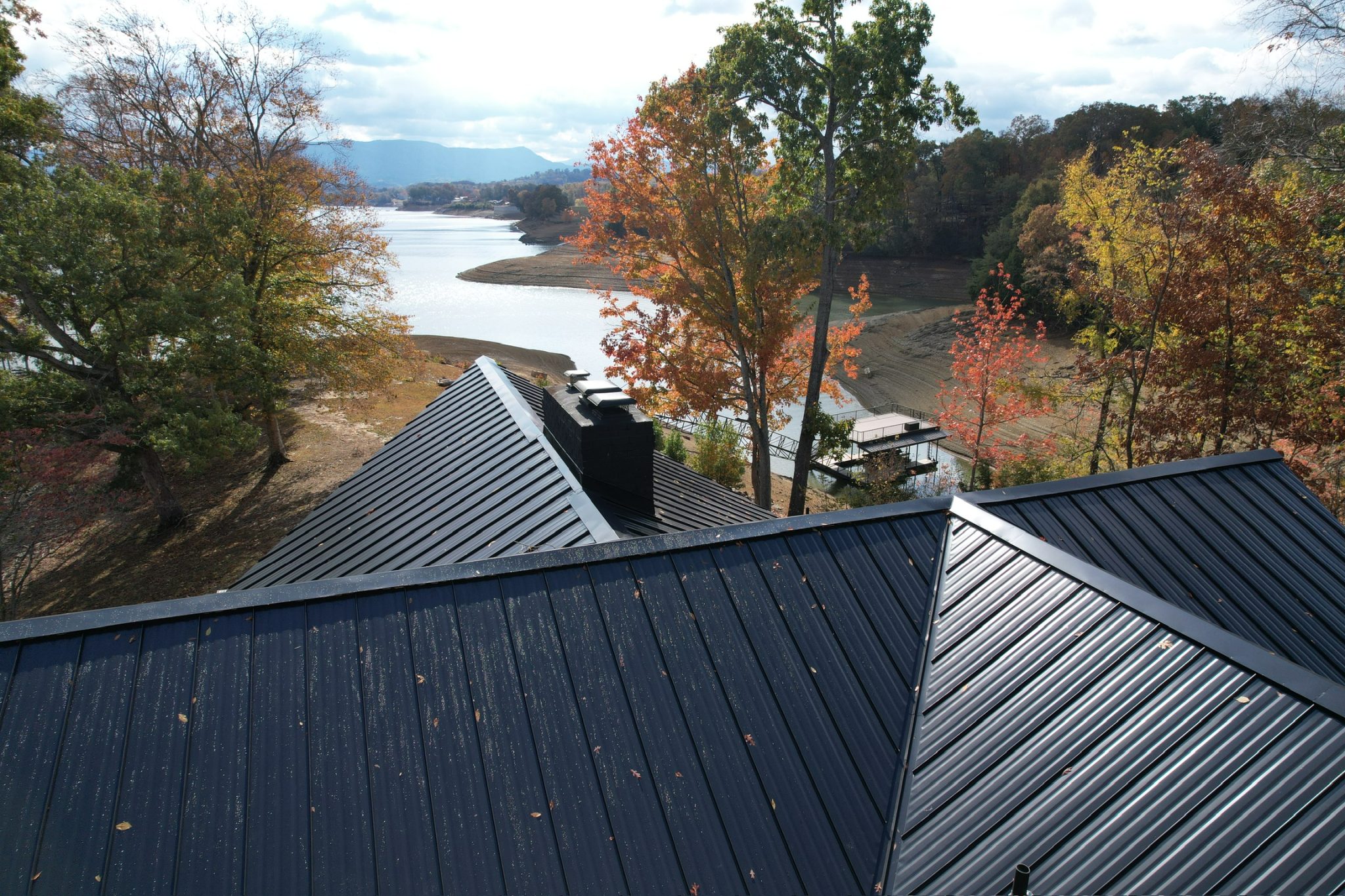 Black standing seam metal roof on an East Tennessee farmhouse overlooking a lake and fall trees