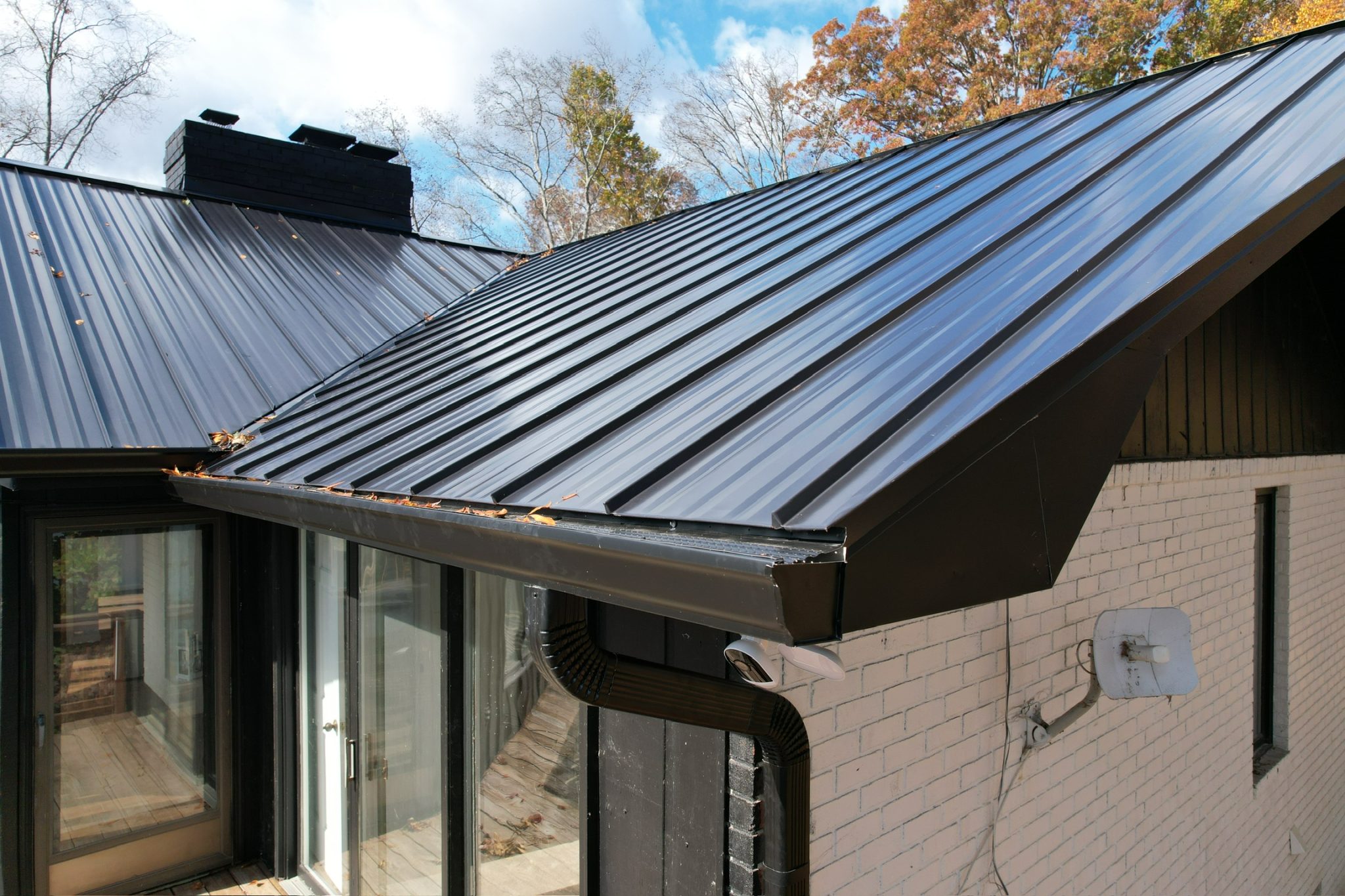 Best gutter colors example with a dark seamless gutter matching a black metal roof and trim on a white brick home.