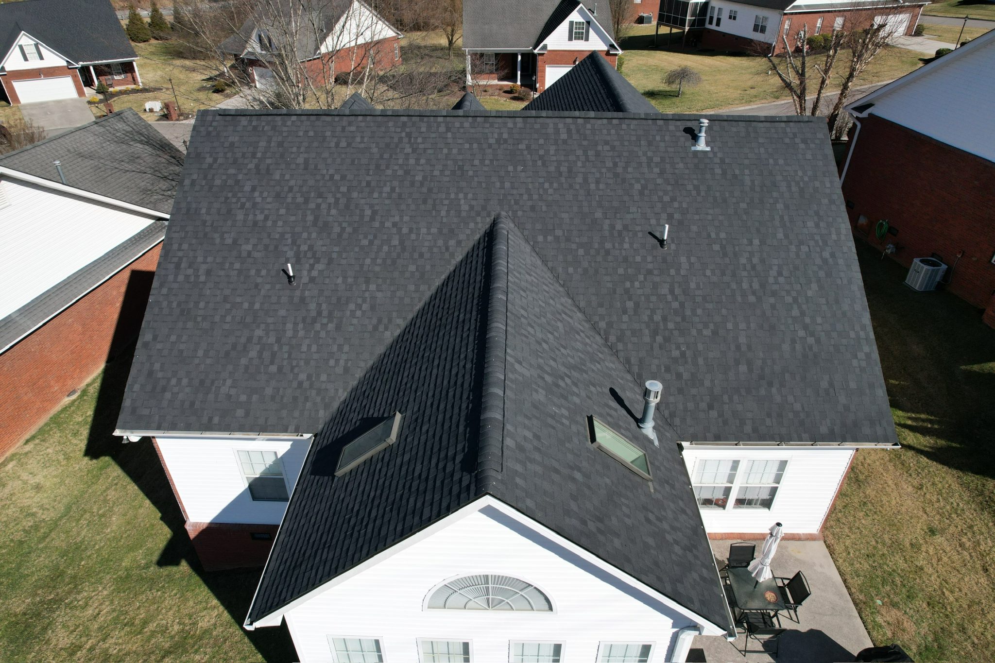 Signs Your Asphalt Roof Is Ready for Asphalt Roof Replacement Aerial view of a home with dark shingles showing a completed asphalt roof replacement.