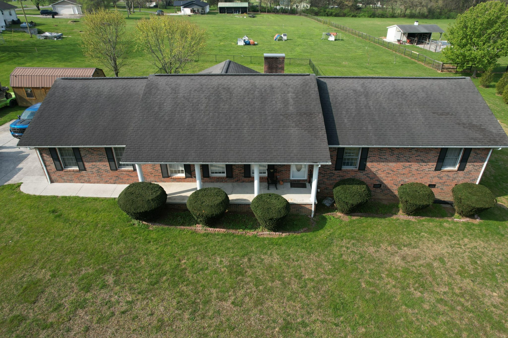 Drone view of a Knoxville brick home with dark asphalt shingles showing roof areas affected by sun exposure.