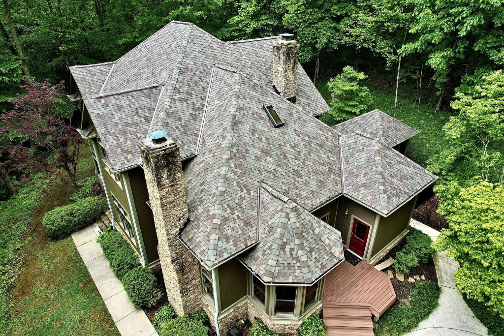 Inspecting Asphalt Roofs for Heat Damage in Knoxville Summers A large brick home with a dark asphalt shingle roof under bright summer sunlight.