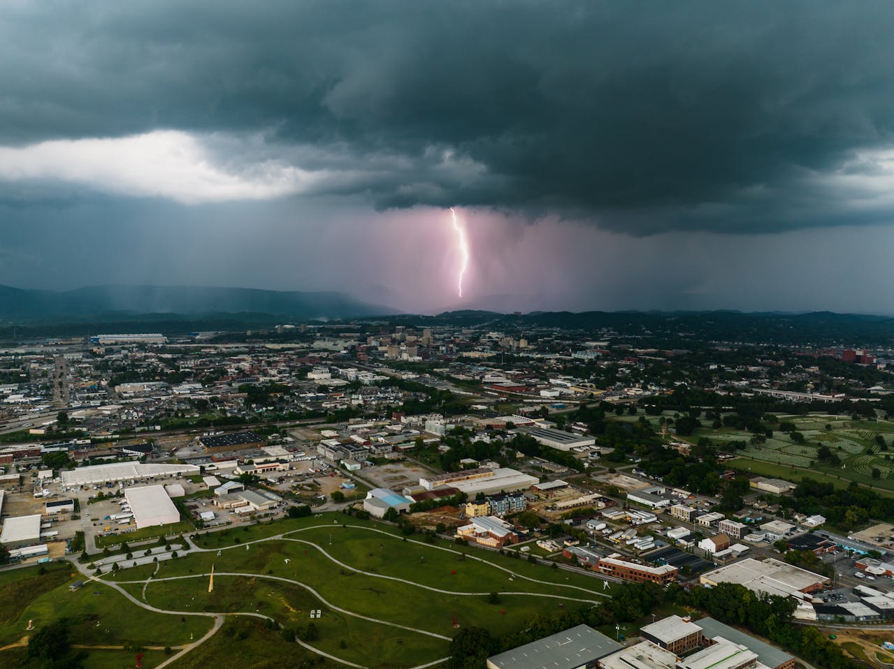 Post-Storm Roof Damage in East Tennessee – What to Do Next Aerial photo of a lightning strike over East Tennessee during a storm, with dark clouds over an urban area and distant hills.